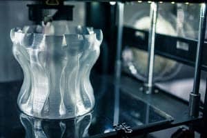 A transparent, wavy-edged object is being meticulously printed inside a 3D printer, showcasing the precision of small format printing.