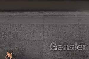 A person is talking on a phone in front of a wall with the word "Gensler" displayed, perhaps discussing small format printing or a web-to-print project.