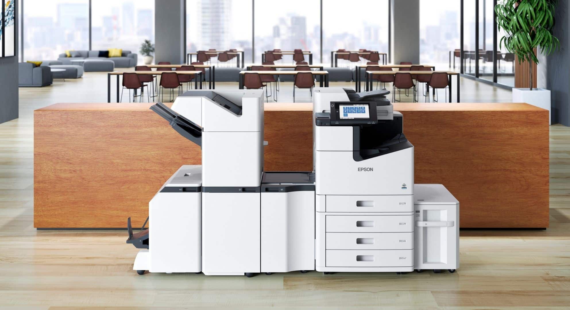 A modern multifunction Epson printer is placed in an office environment with large windows and a city skyline in the background, seamlessly integrating with small format printing tasks.