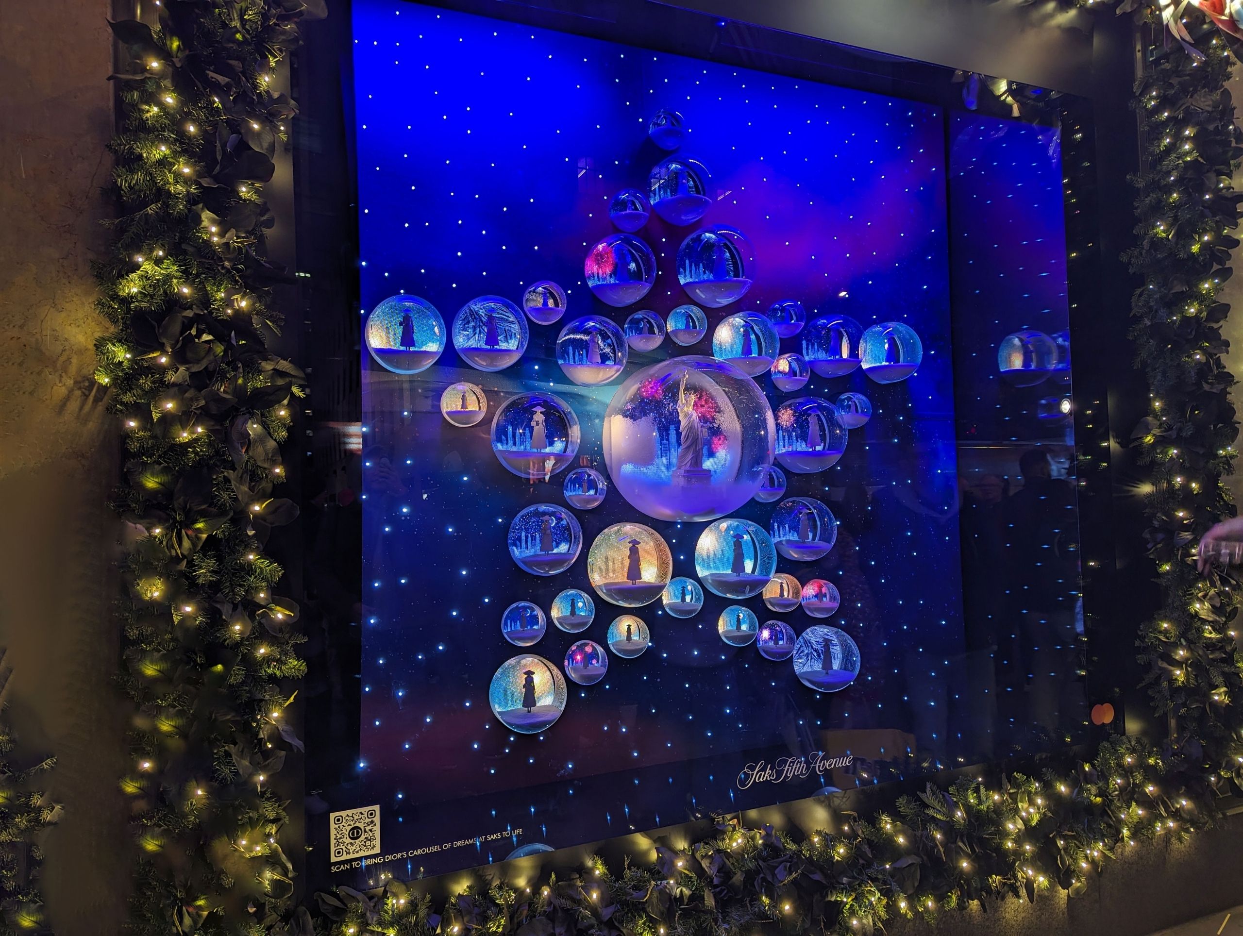 A window display features a star-shaped arrangement of spherical ornaments depicting festive scenes, surrounded by illuminated greenery, enhanced by small format printing for intricate detailing.