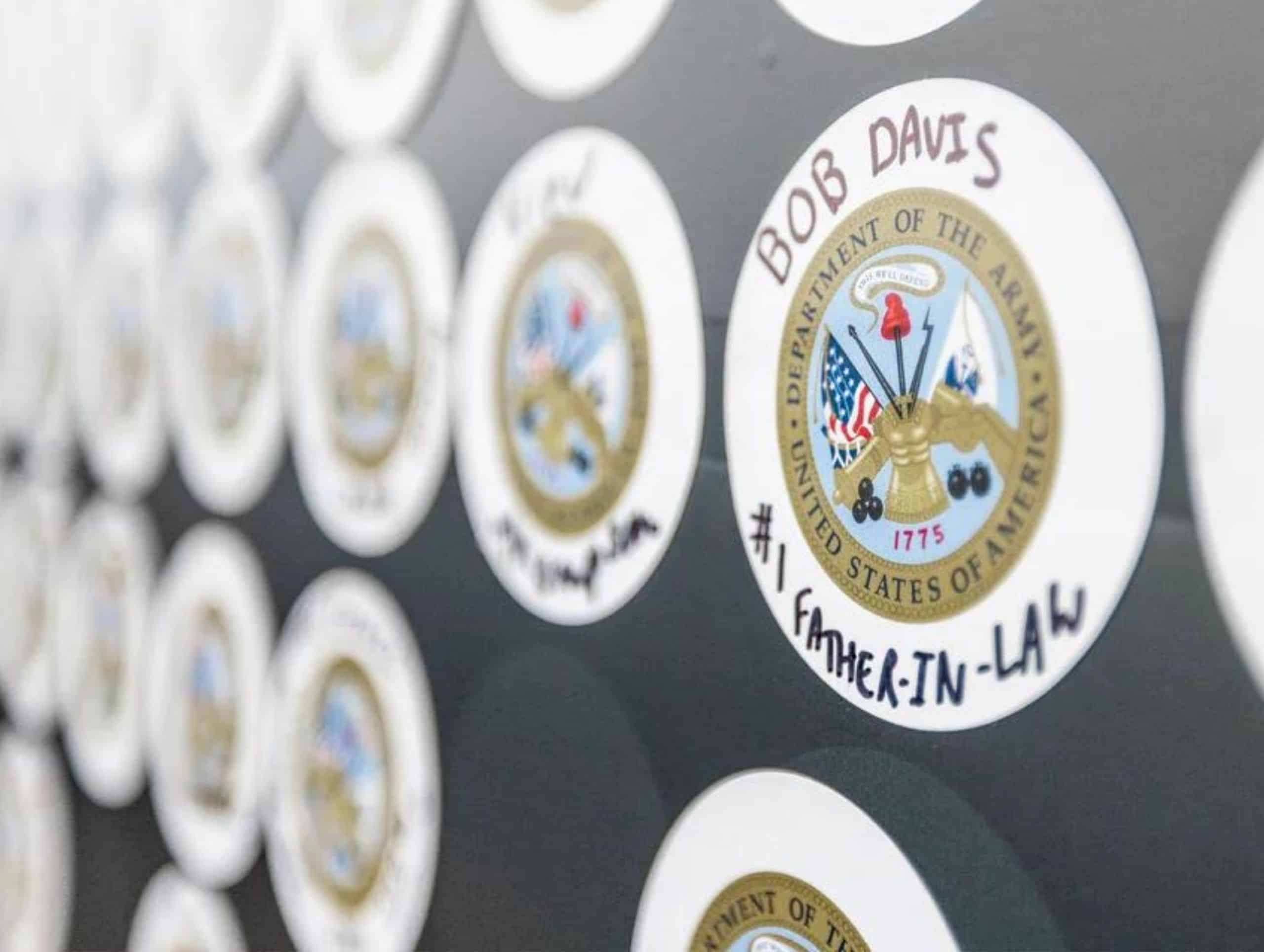 Close-up of a wall displaying multiple U.S. Army emblems, produced through large format printing, with one prominently labeled "Bob Davis #1 Father-in-Law.