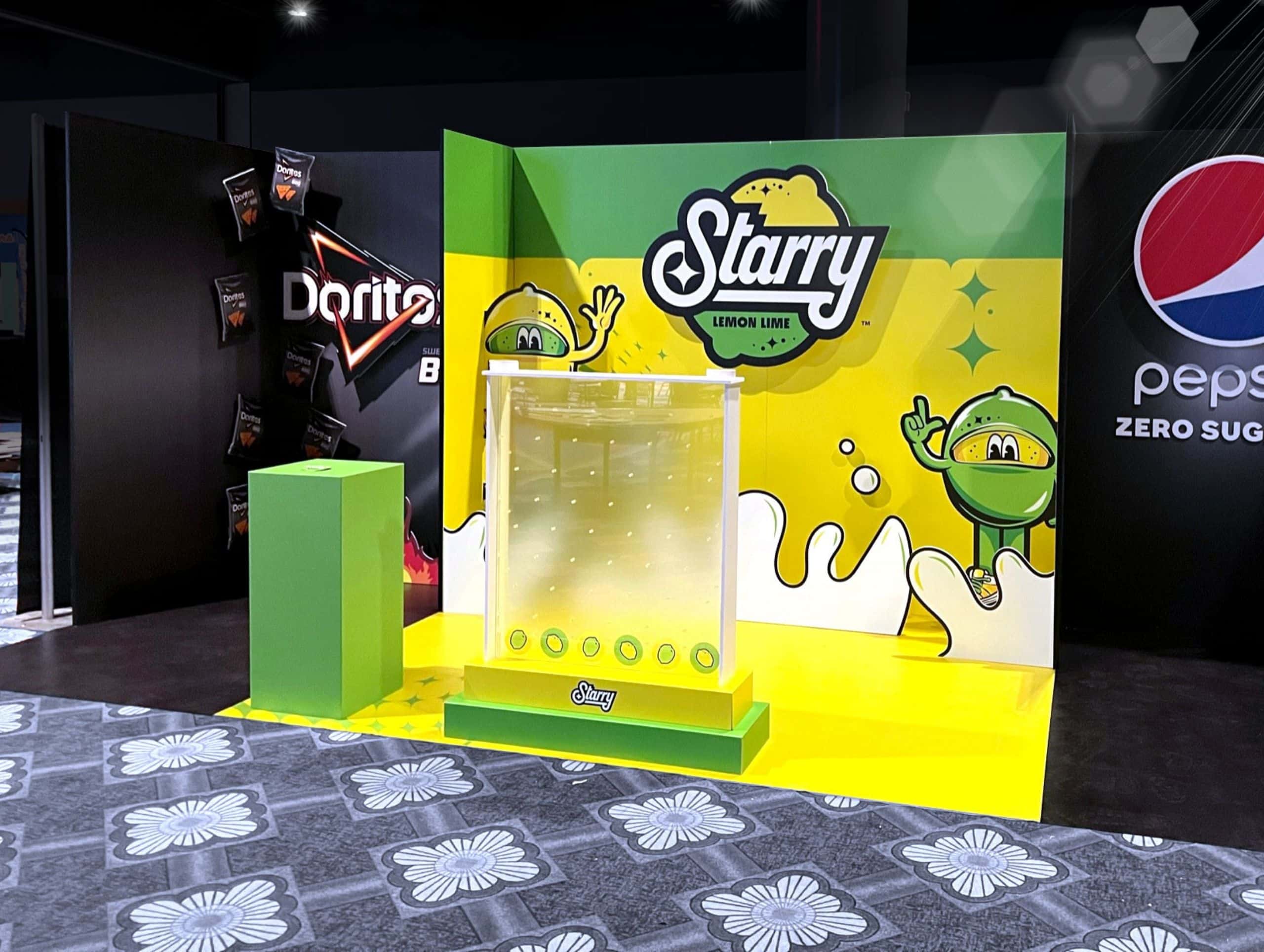 Promotional display featuring Starry lemon-lime soda with branded graphics, brought to life through large format printing. Adjacent signs for Doritos and Pepsi Zero Sugar are visible. The setup includes a small podium and backdrop.