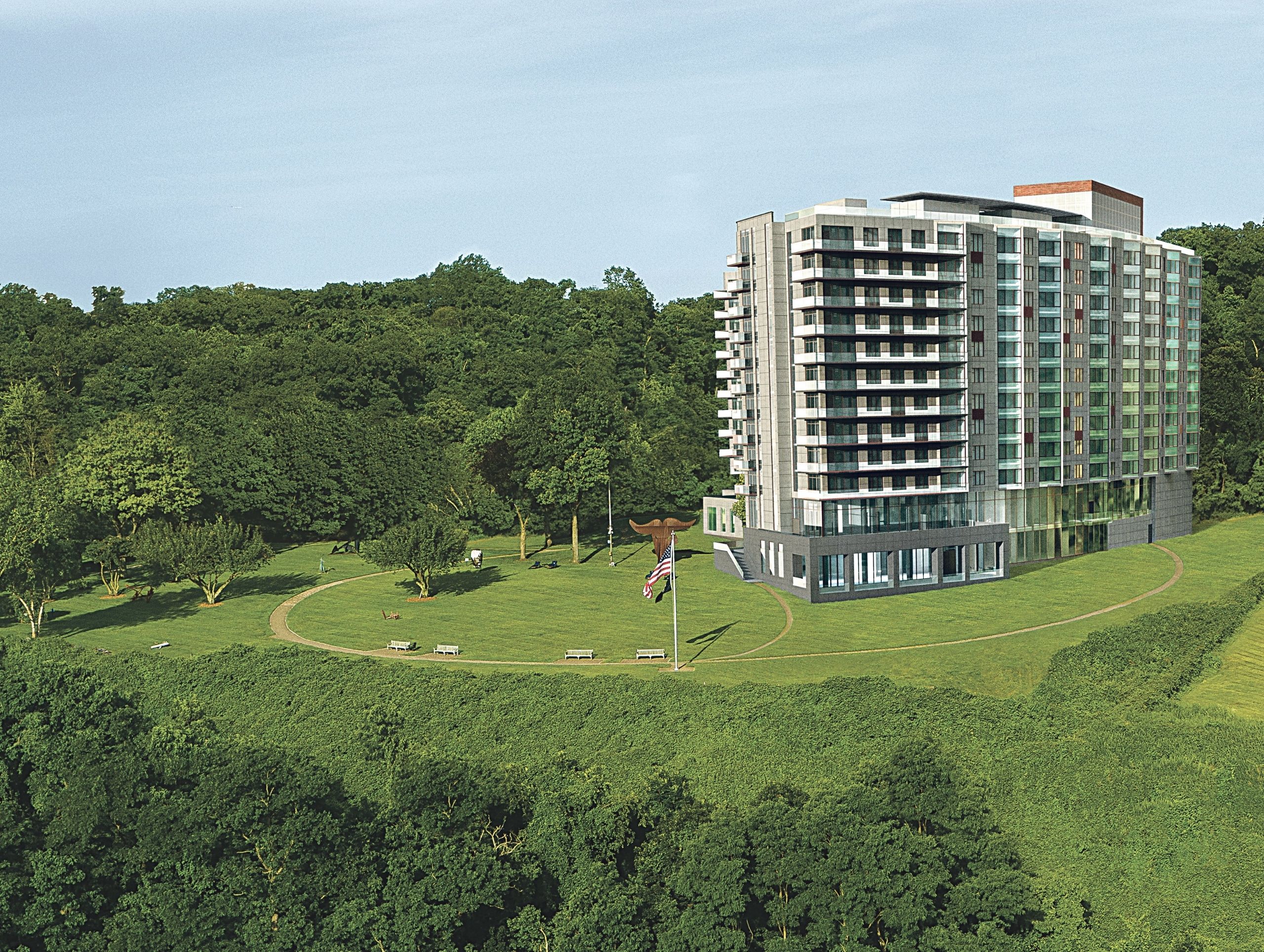 A modern, multi-story apartment building is situated in a large green park with trees in the background and a walking path running alongside. Imagine combining this serene environment with innovative design techniques like 3D printing to create even more unique architectural features.