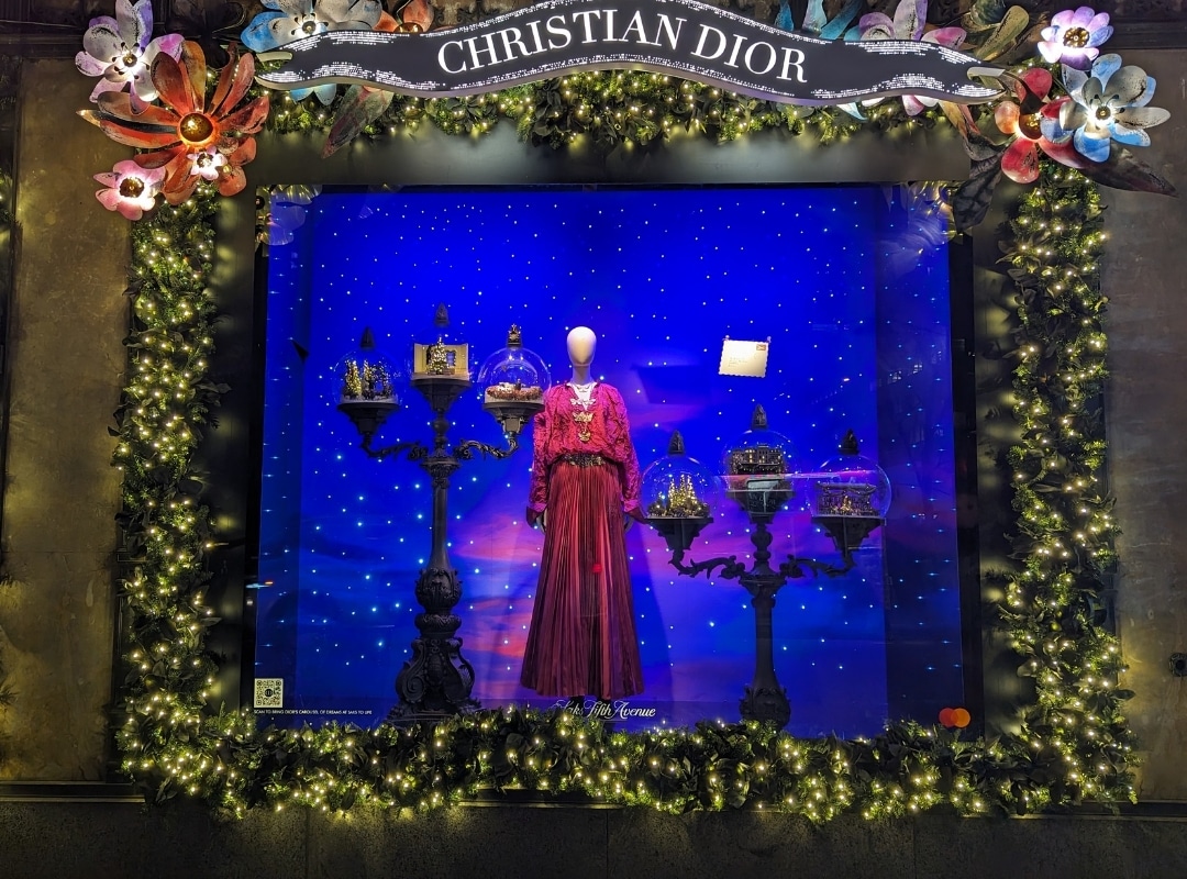 A window display featuring a red dress on a mannequin, surrounded by ornate birdcages, decorative flowers, and lights, with "Christian Dior" signage above. A blue background with a starry pattern brings it all together, enhanced by large format printing for impeccable detail.