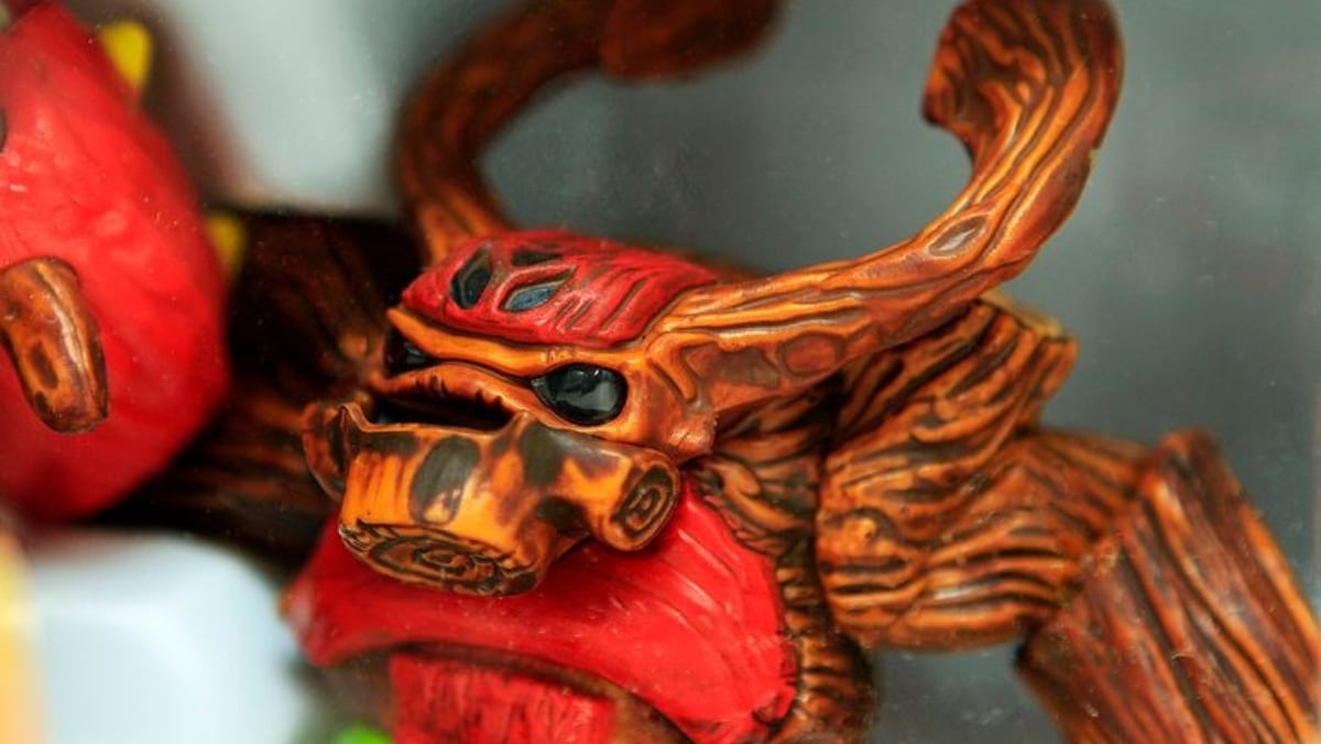 A close-up photo of a small, detailed, orange and red insect-like figurine with black eyes and prominent horns, captured using 3D scanning technology for precise replication.