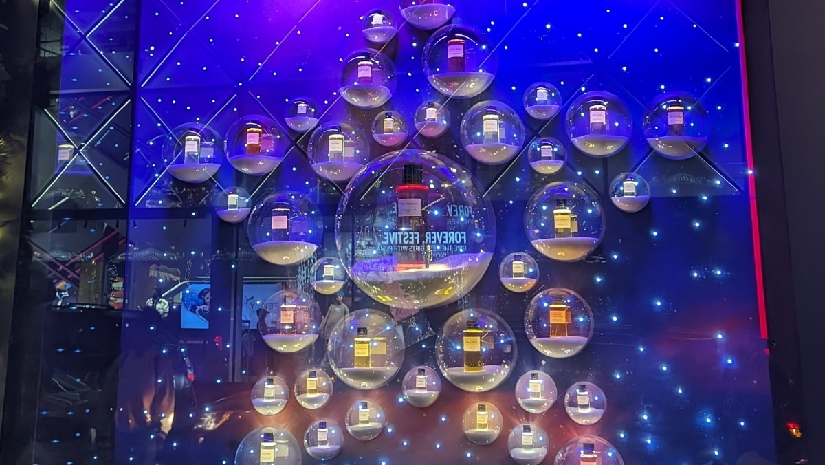 A display with various bottles of fragrance enclosed in clear bubbles, arranged in a geometric pattern against a blue-lit backdrop, evokes the precision and innovation of 3D printing technology.