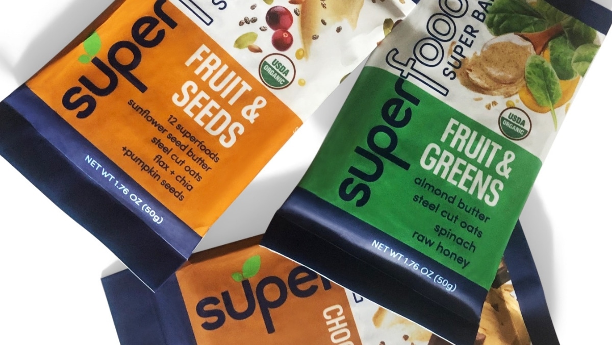 Three packaged snack bars are displayed, labeled "superfood super bar." Flavors visible are Fruit & Seeds, Fruit & Greens, and Chocolate, each in distinct colored packaging created with vibrant small format printing.