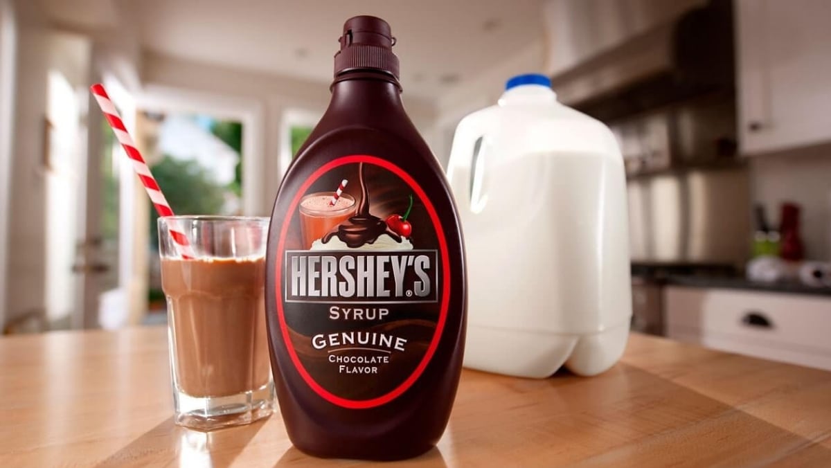 A bottle of Hershey's chocolate syrup, a glass of chocolate milk with a straw, and a gallon of milk are on the kitchen counter, ready to be captured by 3D scanning technology for precise small format printing.