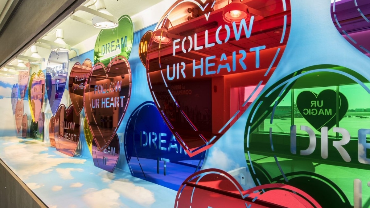 Colorful heart-shaped signs with messages like "FOLLOW UR HEART" and "DREAM" are displayed on a glass wall in a brightly lit room, showcasing the stunning precision achieved through 3D printing.