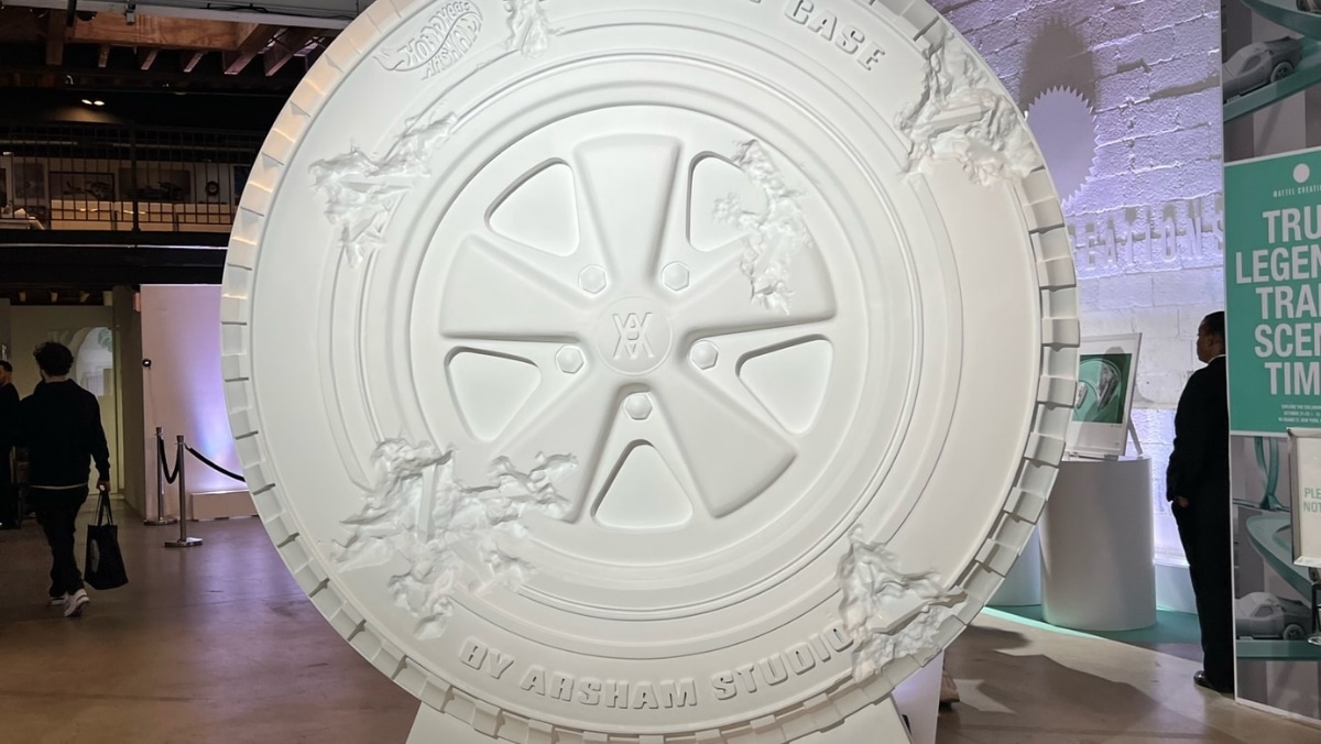 A large, round, detailed sculpture resembling a wheel, created by Arsham Studio, displayed indoors with people and informational panels in the background. The intricate design mirrors the precision typically seen in large format printing.