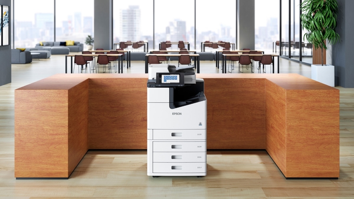 A multi-function printer, equipped with 3D scanning capabilities, stands in a modern office environment with large windows, light wooden tables, and chairs.