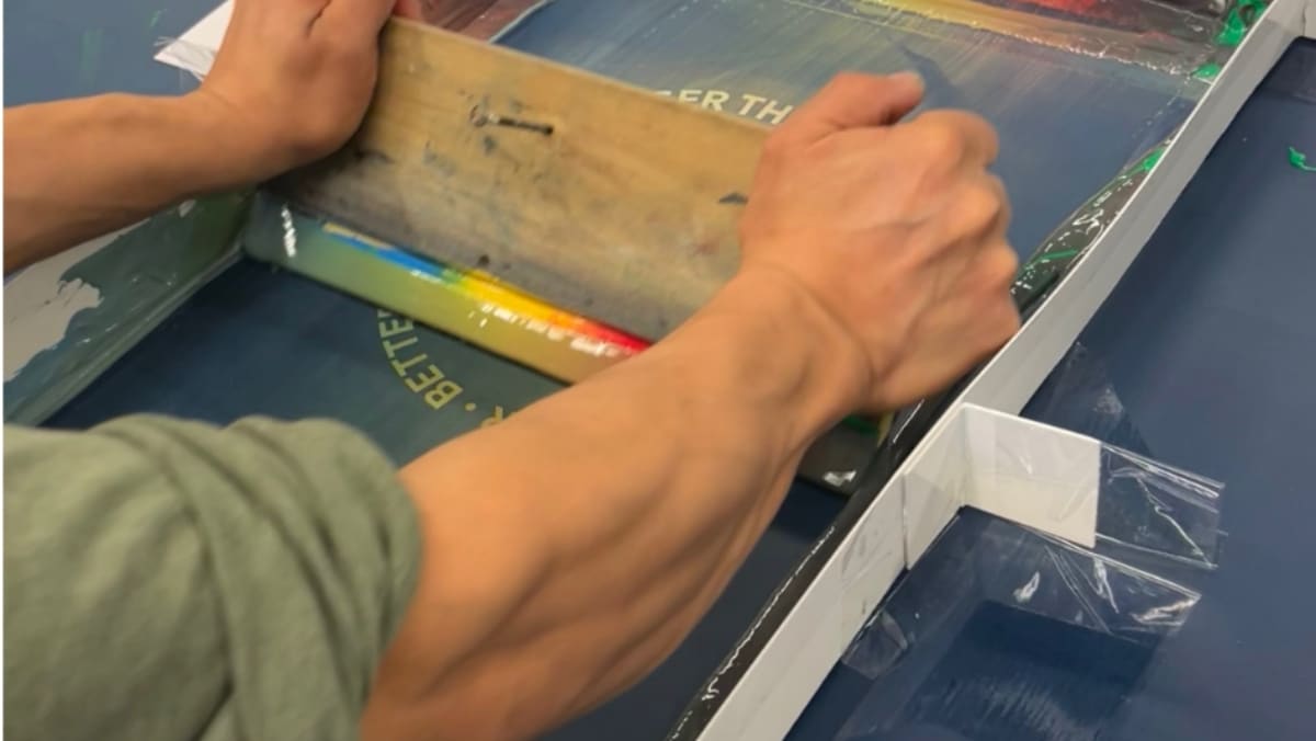 A person uses a squeegee to spread rainbow-colored ink on a screen printing frame, seamlessly integrating traditional art with the latest in large format printing techniques.