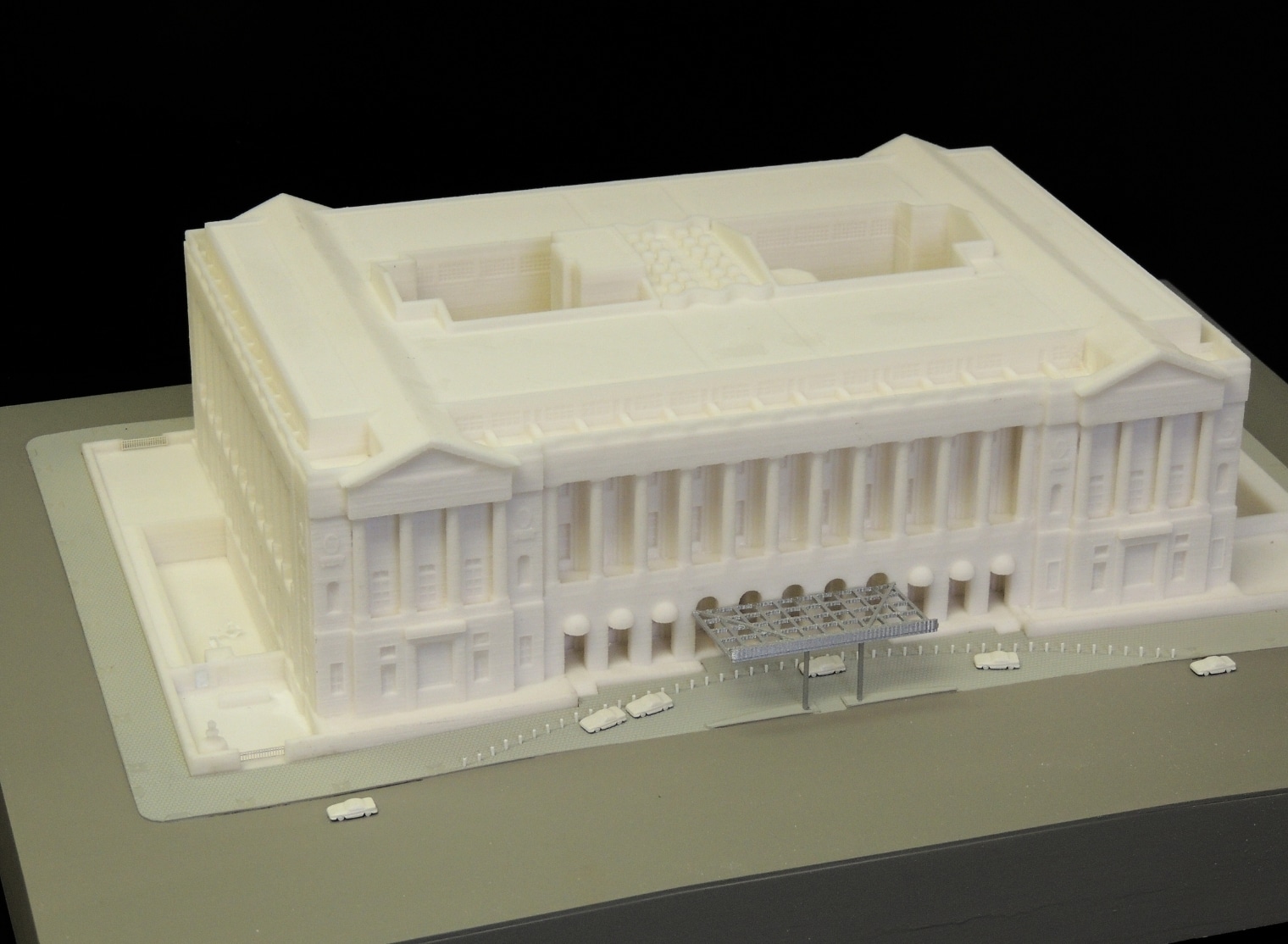 A 3D model of a large rectangular building with columns at the front and small vehicles surrounding it, made even more precise through advanced 3D scanning technology.