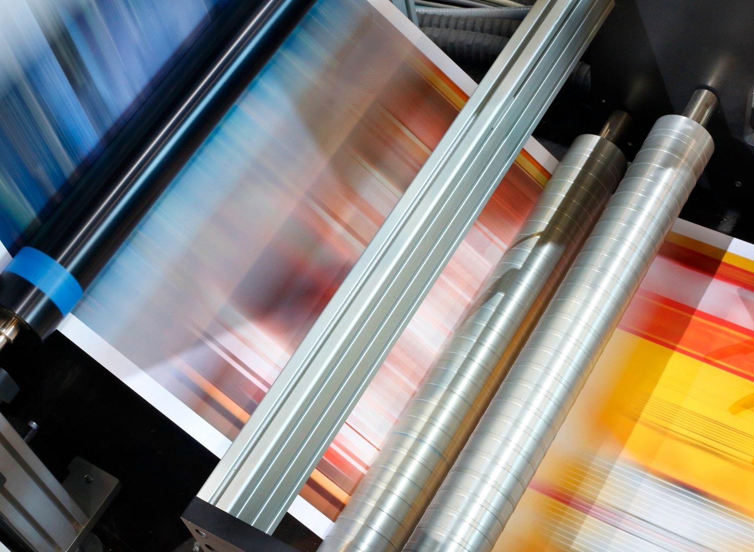 Close-up of a large format printing machine in operation, with colorful sheets being printed and processed through various rollers.