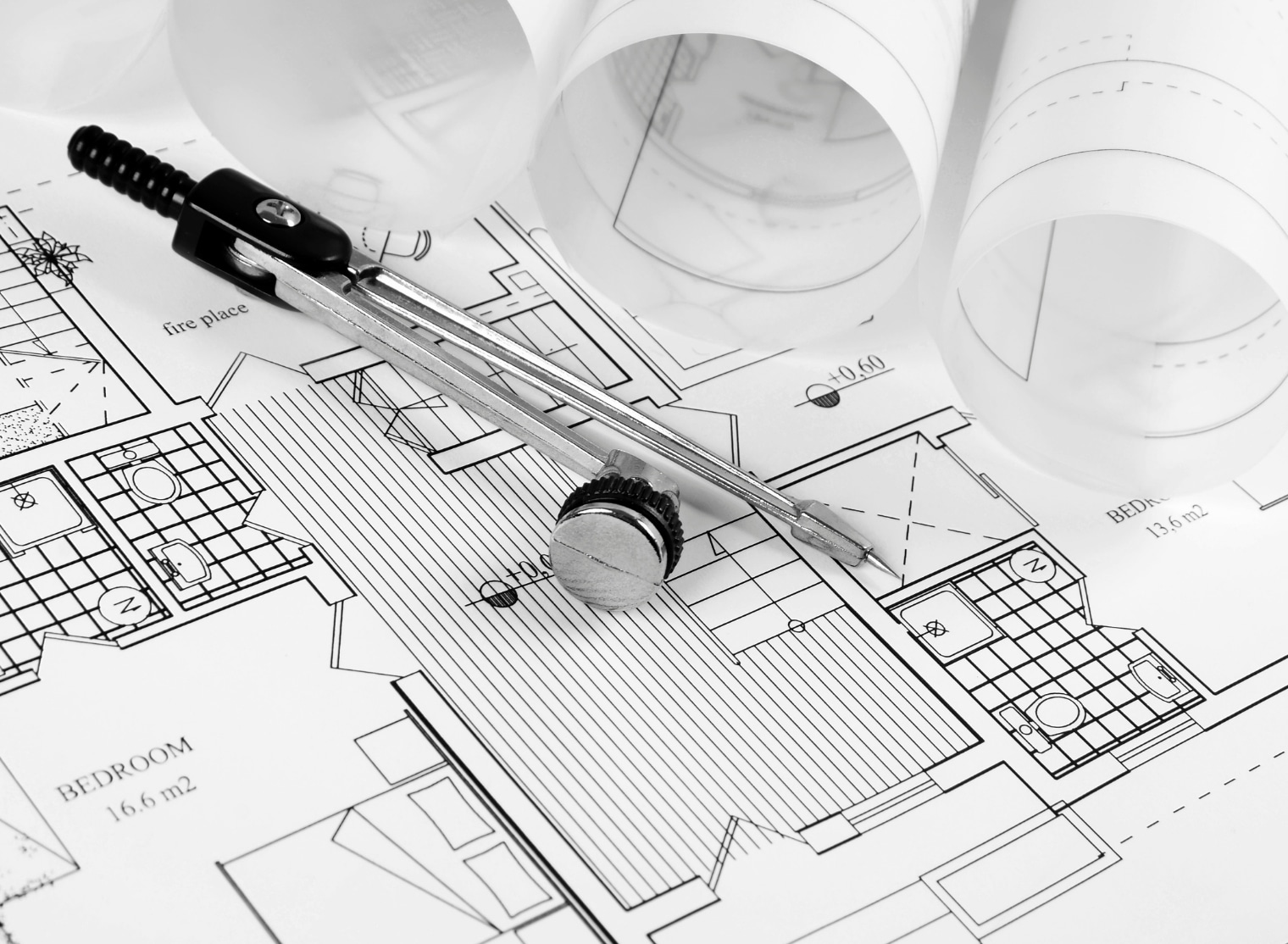 A pair of compasses lying on a detailed architectural floor plan, surrounded by rolled-up blueprints and hints of large format printing techniques.