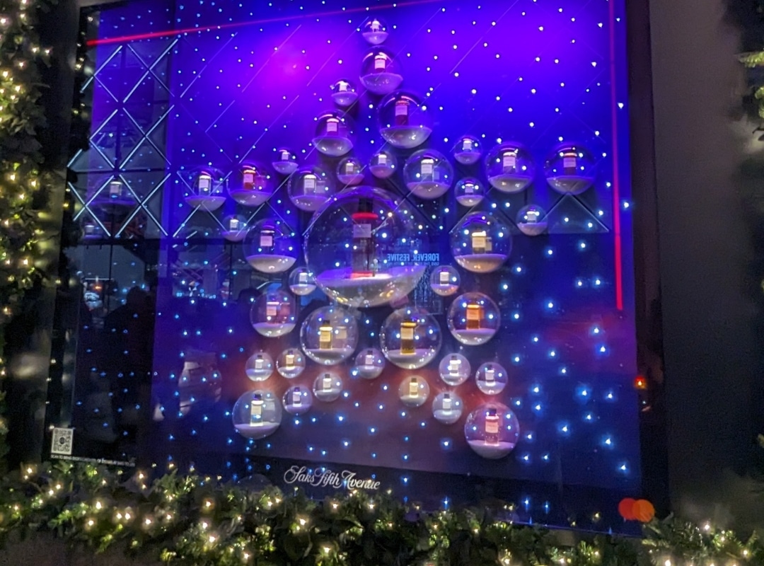 A display features a large star shape with lights, holding several shelves with perfume bottles. The background is illuminated with blue and purple lights. Garland decorates the frame's lower edge, bringing a touch of 3D printing innovation to the festive design.