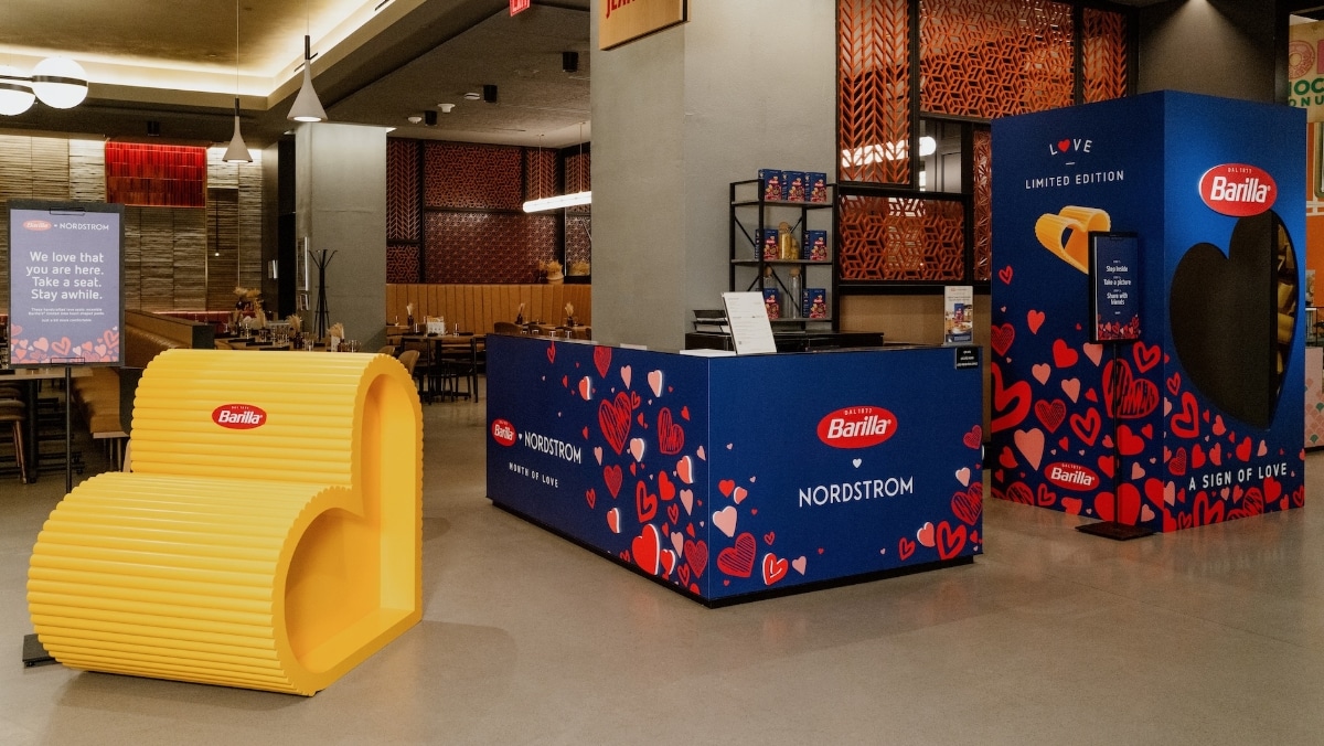 Indoor display featuring Barilla and Nordstrom collaboration. Includes a large pasta-shaped seating area, branded booth, and a heart-shaped structure adorned with hearts and logos. The exhibit showcases innovative 3D printing techniques, enhancing the visual impact of the design elements.