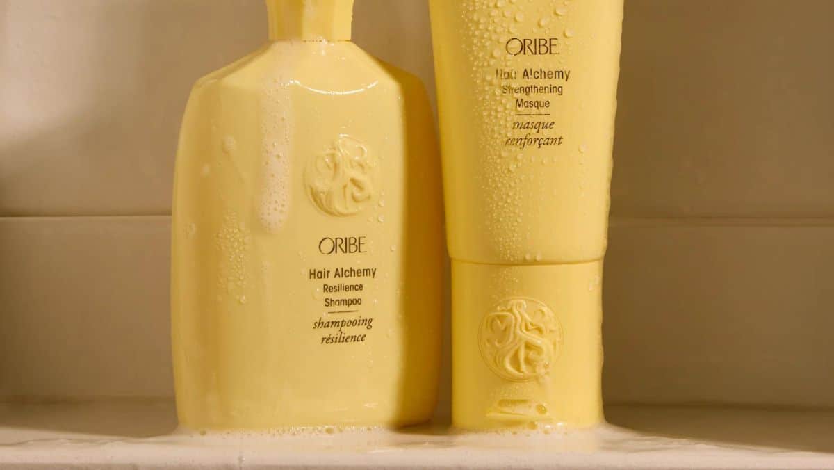 Two yellow Oribe Hair Alchemy bottles, one shampoo and one strengthening masque, with water droplets on them, evoke a sleek design reminiscent of innovative 3D scanning services.