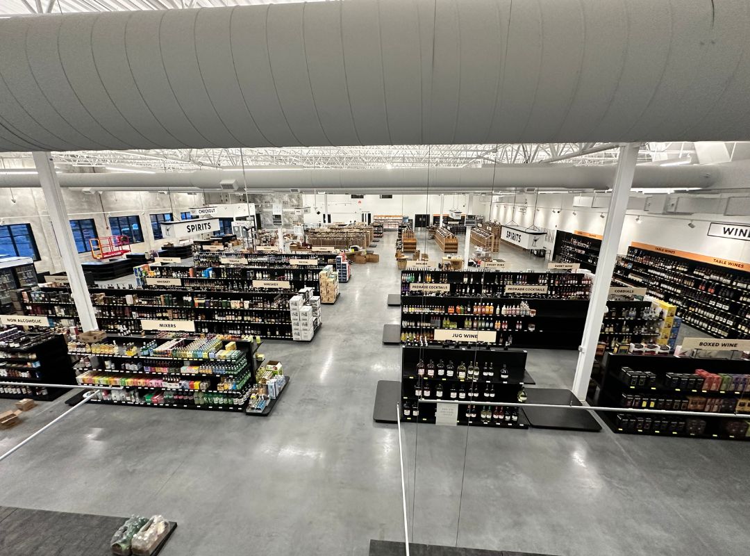 View of a large liquor store interior with rows of shelves stocked with various bottles, a wide aisle, and high ceilings, seamlessly integrated with managed IT services for efficiency and enhanced customer experience.