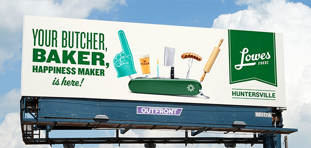 Billboard displays "Your Butcher, Baker, Happiness Maker is here!" with kitchen utensils and foods popping out of a toaster. Alongside the Lowes Foods logo and "Huntersville" text on the right side, it highlights their new 3D services, adding a modern twist to your shopping experience.