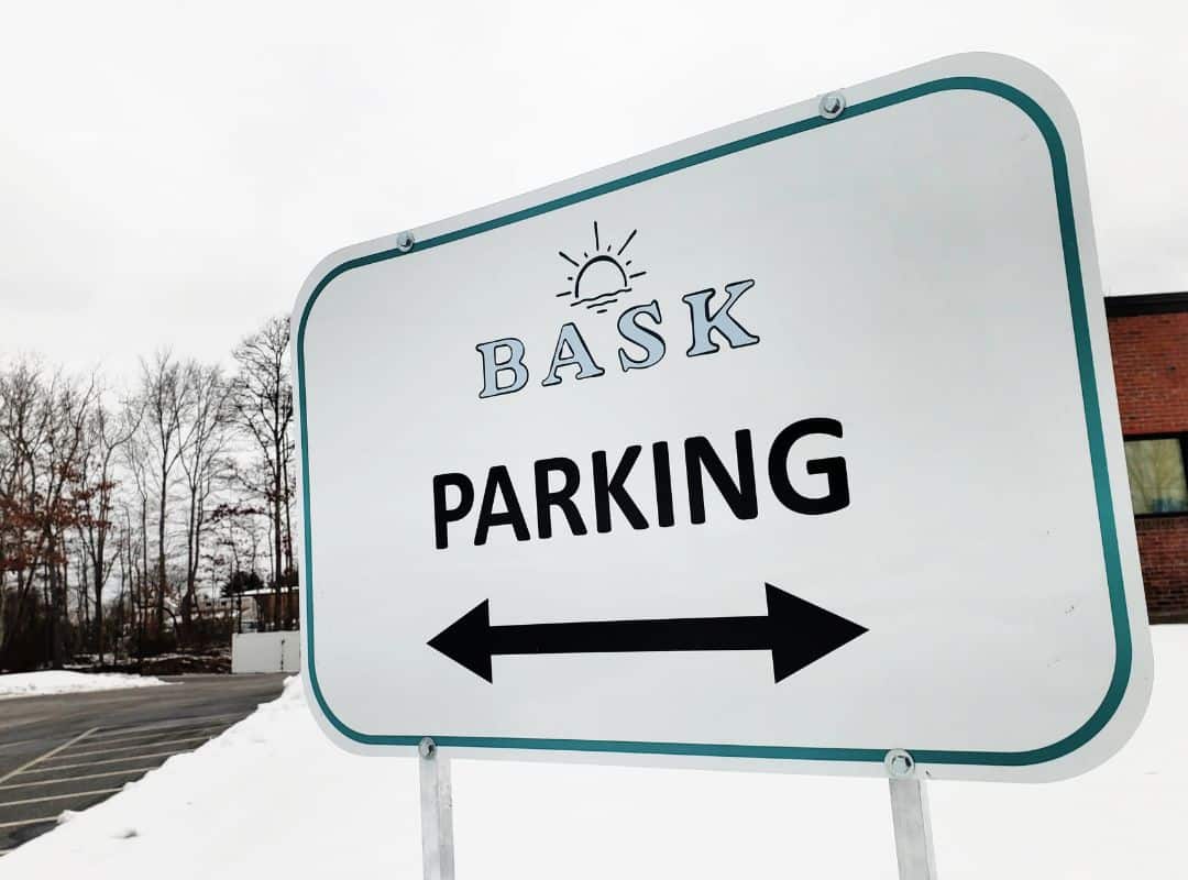 A sign reading "Bask Parking" with arrows pointing in both directions, set against a snowy backdrop with trees and a building, evokes a scene as precise as 3D scanning services.