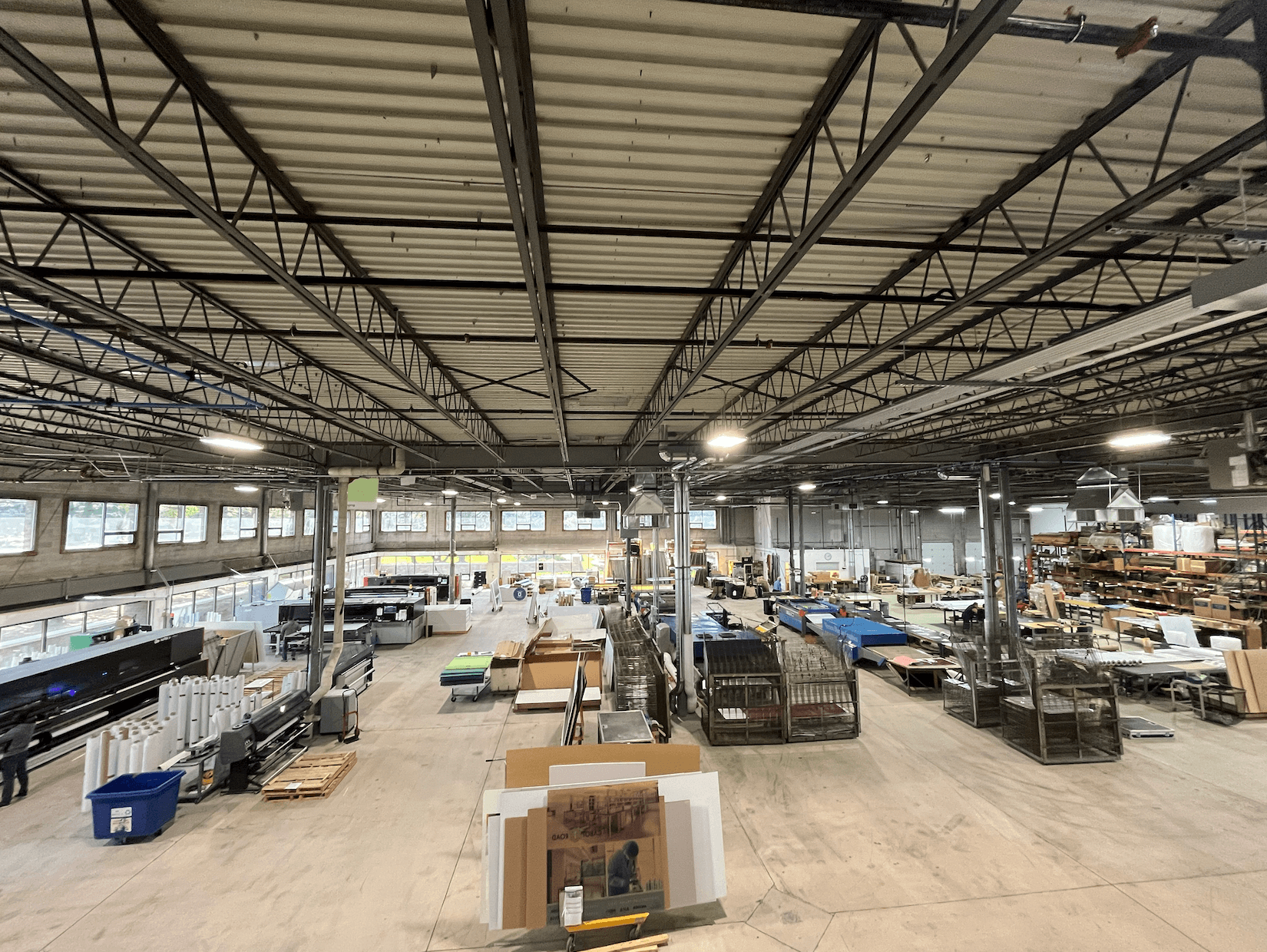 Wide-angle view of a large warehouse with high ceilings, stacked materials, and various equipment. Shelves and workstations are organized throughout the space, optimized with 3D scanning services to streamline inventory management.